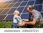 Small photo of Little son and father saving money together, putting cash into piggy bank. Dad teaching little kid how to save money for future, putting their savings into piggybank on background of solar panels.