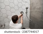 Small photo of Back view of male plumber installing wall mounted shower system in apartment under renovation. Man repairing metal shower faucet handle while working on bathroom renovation. Plumbing works concept.