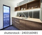 Modern kitchen with white walls and glass door with scenic view inside. Side view of kitchen area with wooden shelves and working surface, illuminated with warm LED light indoor. Concept of interior.