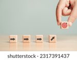 Small photo of Arrow leading point to target icon on wooden blocks with businessman hand placing red goal dartboard symbol. Business agenda and mission setting concept. Dart board cube future vision strategy success