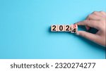 Small photo of 2024 Happy New Year eve wooden blocks flip change hand blue background. Countdown starting ending 2023 action schedule calendar strategy future vision. Business startup plan resolution celebration
