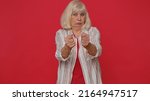 Small photo of Greedy senior woman showing fig negative gesture you dont get it anyway. Rapacious, avaricious, acquisitive. Body language. Refusal fig sign. Elderly grandmother isolated on red studio wall background