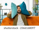 Small photo of Repair work at neighbors. Irritated arabian man cover ears with pillows annoyed by noisy loud music neighbors suffer from headache wishes silence. Thin walls at home flat without sound insulation