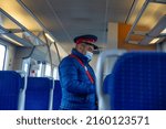 Small photo of 20 April 2022 Train ticket collector with cap and jacket walking through blue seats on the fast train from Bucharest to Henry Coanda airport