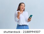 Small photo of Excited young Asian woman using mobile phone gesturing yes with raised fist reacting to online news isolated over white background