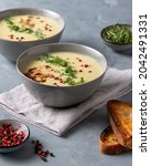 Small photo of Cauliflower soup on gray tabletop, creamy flower soup with toasted bread, garden cress, red and black peppercorns.