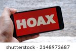Small photo of Hand holding smartphone with letter HOAX on red background. Propaganda, disinformation and hoax concept.