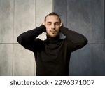 Small photo of Young man with closed eyes covering his ears in an effort to block out the sound around him. Conceptual image of struggle with deafness and feeling disconnected from society