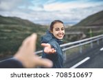 Young laughing girl outstretching hand asking to follow her on background of mountain road, Iceland, West Fjords.
