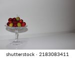 Front view of luscious red plums and green plums on a glass serving platter on a white table and in front of a white background