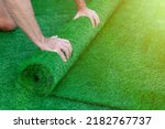 Small photo of Selective focus on a man's hands unrolling a roll of artificial turf. Easy laying of artificial green grass