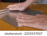 Small photo of Men hands roll off the aluminum foil for household use on a wooden surface.