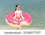 Small photo of Cute little child in beachwear with bright inflatable ring on a city lake. Summer vacation in a city. Holiday concept