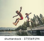 Kids jumping off the dock into a beautiful mountain lake. Having fun on a summer vacation at the lake with friends