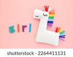 Crochet amigurumi handmade stuffed soft white unicorn toy with rainbow mane and word Girl on pink background. Handwork hobby. Craft diy newborn pregnancy concept. Knitted doll for little baby. Flatlay