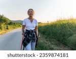 a recreational hiker uses walking sticks while walking on a country road, young asian woman enjoying her country side holiday