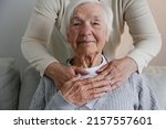 Small photo of Unrecognizable female expressing care towards an elderly lady, hugging her from behind holding hands. Two adult women of different age. Family values concept. lose up, copy space, background.