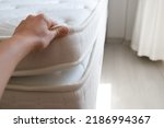 Small photo of Cropped shot of woman showcasing the top of white orthopedic mattress. Female showing hypoallergenic foam matress protector. Close up, copy space, top view, background.