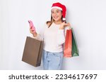 Cheerful young Asian woman wearing Christmas hat holding shopping bags and mobile phone isolated on white background. Happy New Year Christmas 2023