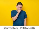 Small photo of Professional young Asian male doctor or nurse wearing a blue uniform feeling unwell and coughing isolated on yellow background. Healthcare medicine concept