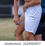 Small photo of A caucasian male athlete self treats a groin strain with painkilling analgesic spray directing a jet of freezing cold liquid mist up the leg of his white shorts.