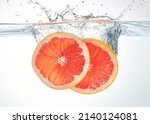 Small photo of Two slices of fresh red grapefruit being splashed into water. Beautiful juicy piece of citrus grapefruit taking a plunge into water. Fresh natural orange citrus flavour.
