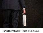 Small photo of A man in a suit with a suitcase handcuffed on a black background, close-up, selective focus, dark tonality. Concept: secure delivery of money and documents, business courier, classified information.
