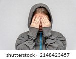 Small photo of A teenage girl is handcuffed, hiding her face, in a hoodie, on a gray background. Juvenile delinquent, criminal liability of minors. Members of youth criminal groups and gangs.