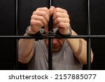 Small photo of A man in handcuffs in a cell behind bars. Concept: a prisoner in a courtroom, a court sentence to a convicted person, a prison term.