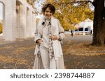 attractive smiling woman walking in autumn park wearing beige trench and white knitted scarf, winter cold season accessories trend, stylish outfit, elegant beautiful lady with short haircut
