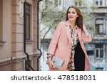young beautiful stylish woman walking in street in pink coat, floral printed dress, holding silver purse in hands, autumn fashion trend, smiling, happy