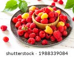 Ripe juicy sweet berries of yellow and red raspberries on a white rustic table. 