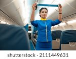 Small photo of Woman stewardess in air hostess uniform holding safety belt while standing near passenger seats in airplane salon