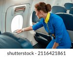 Woman stewardess in air hostess uniform standing near passenger seat and looking out aircraft window