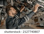 Bearded young man aviation mechanic checking aircraft components while working in repair station