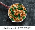 One pot lunch. Orzo pasta with meatballs and spinach in tomato sauce in a frying pan on a dark background, top view    