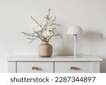 Small photo of Minimalism style interior decor - flower arrangement in a ceramic vase and a white metal table lamp on a white table