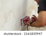 Small photo of Image of the hands of a handyman who removes plaster and mold from a wall with a sanding machine. Reference to problems of humidity