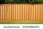 Small photo of Frontal shot of a wooden picket fence with a green hedge in the background and grass in the foreground. Pale wood. Copy space