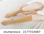 Knee socks or socks. Beige compression stockings on a woman in a white room. Girl putting on stockings at home. Beautiful female legs.