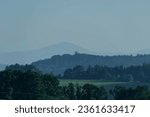 Sudetes foreland. The undulating terrain is covered with farmlands, meadows and forests. On the horizon you can see the peaks of the Sudetes Mountains, hidden in the fog and very blurred.
