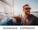 Small photo of Man dressed in casual wear and sunglasses on a yacht. Happy adult bearded yachtsman close-up portrait. Handsome sailor on a boat smiling during regata on a sea or river.