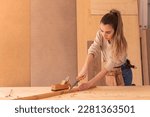 Small photo of Craftswoman carving wood with chisel. Concentrated female joiner in apron gouging wood with chisel near jack plane