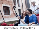 Smiling couple taking self-portrait digital camera in gondola on canal in venice