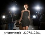 Celebrity in black dress arriving at event being photographed by paparazzi