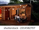 Happy couple friends enjoying dinner, toasting wine glasses at summer table on house patio with string lights