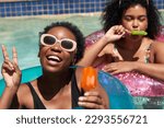 Two Black friends pose in the swimming pool eating ice lolly popsicle
