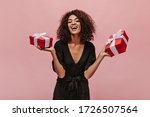 Attractive stylish girl with curly cool hairstyle in polka dot dark clothes laughing, looking into camera and holding gift boxes.