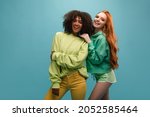 Small photo of Red-haired girl in short shorts stands sideways next to frankly smiling dark-skinned brunette. They have fun together. Interracial friendship concept