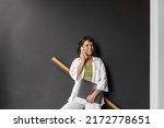 Pretty caucasian young brunette woman uses smartphone standing against black wall. Business lady is holding closed laptop. Freelance work, people concept